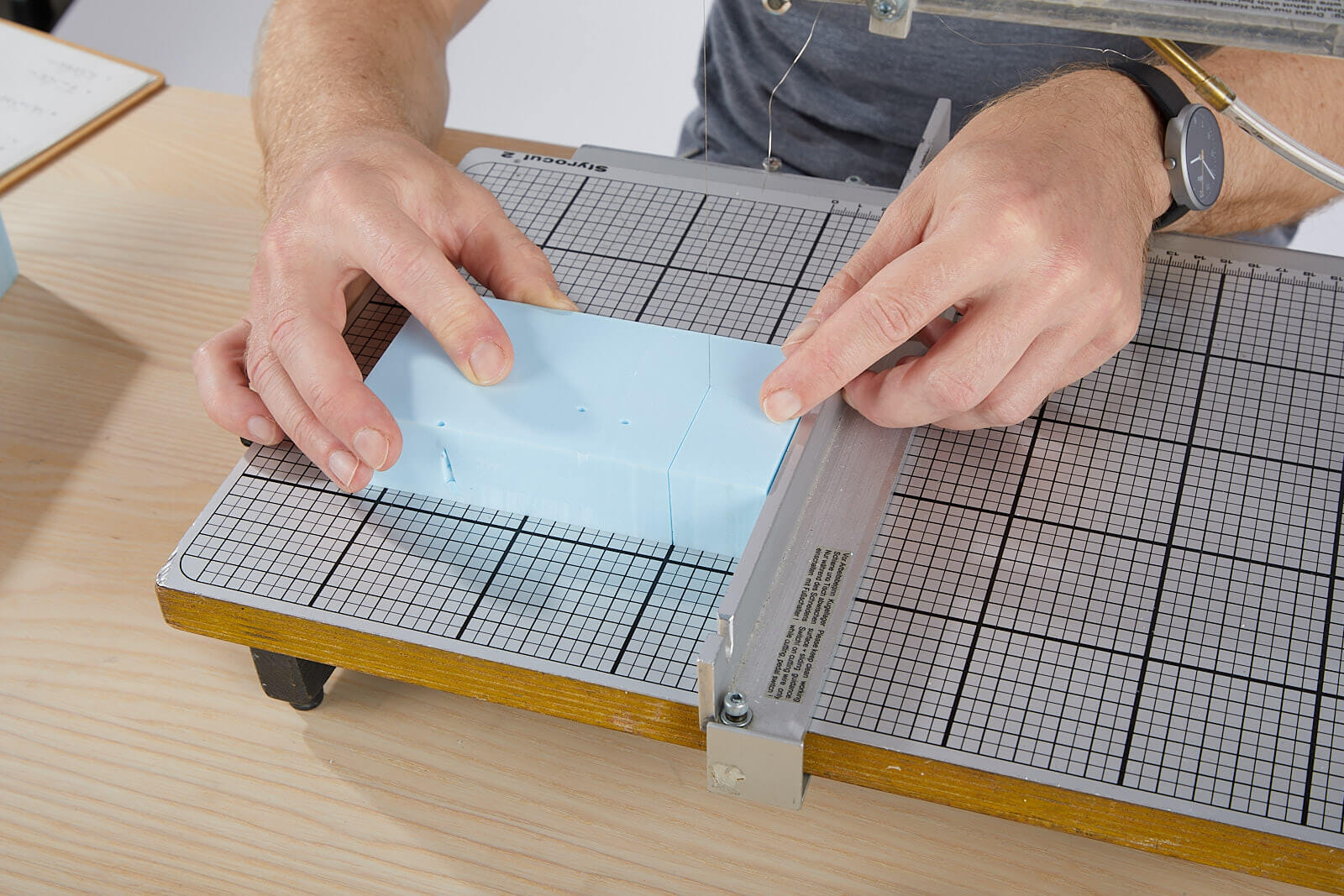 Styrofoam an Heißdrahtsäge schneiden ein hellblauer Quader Styrofoam wird mit einer Heißdrahtsäge entlang eines Anschlags gerade und rechtwinklig geteilt.