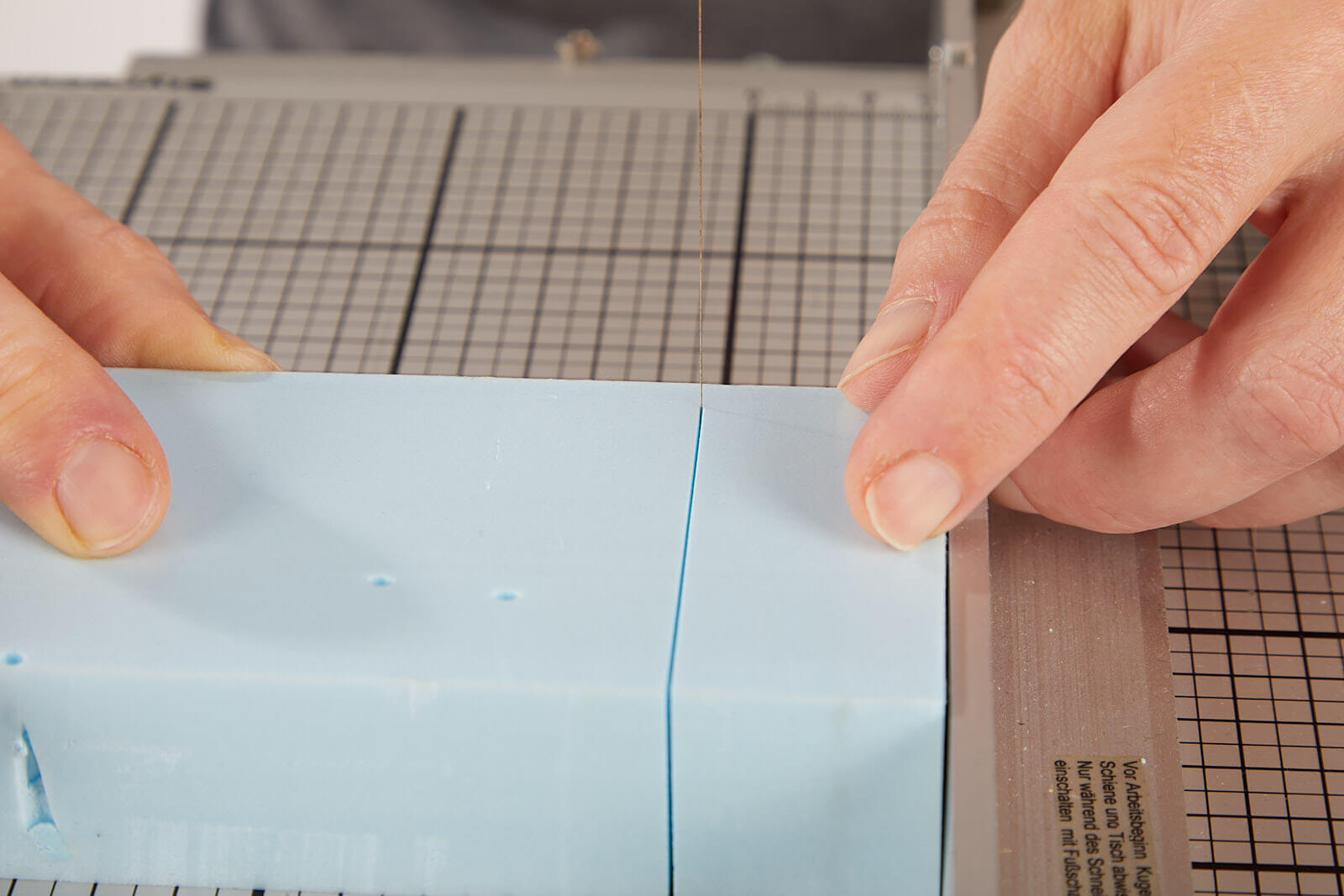 Styrofoam an Heißdrahtsäge schneiden 2 ein hellblauer Quader Styrofoam wird mit einer Heißdrahtsäge entlang eines Anschlags gerade und rechtwinklig geteilt. (andere Perspektive, Schnitt bereits fast durch den gesamten Quader.)