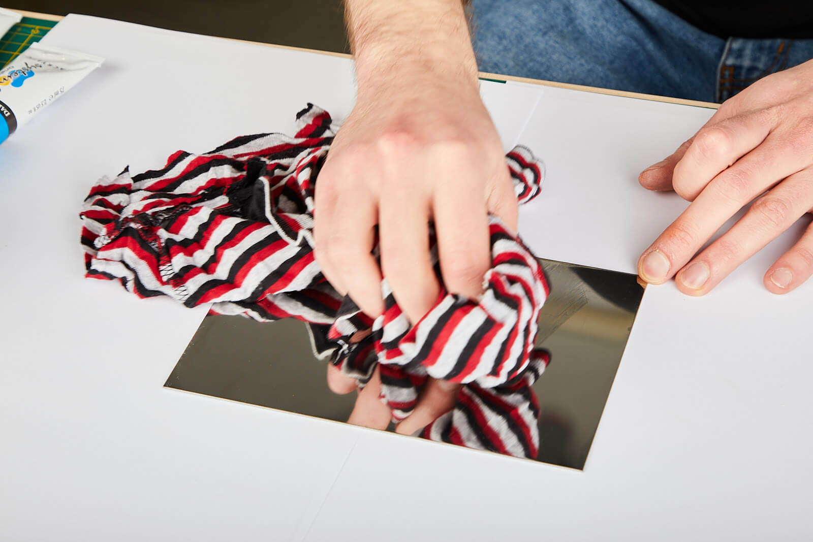 Entfetten der Blechoberfläche eine Hand wischt mit einem Lappen über ein kleines Stück Edelstahlblech. Im Lappen ist Benzin zum Entfetten der Oberfläche.