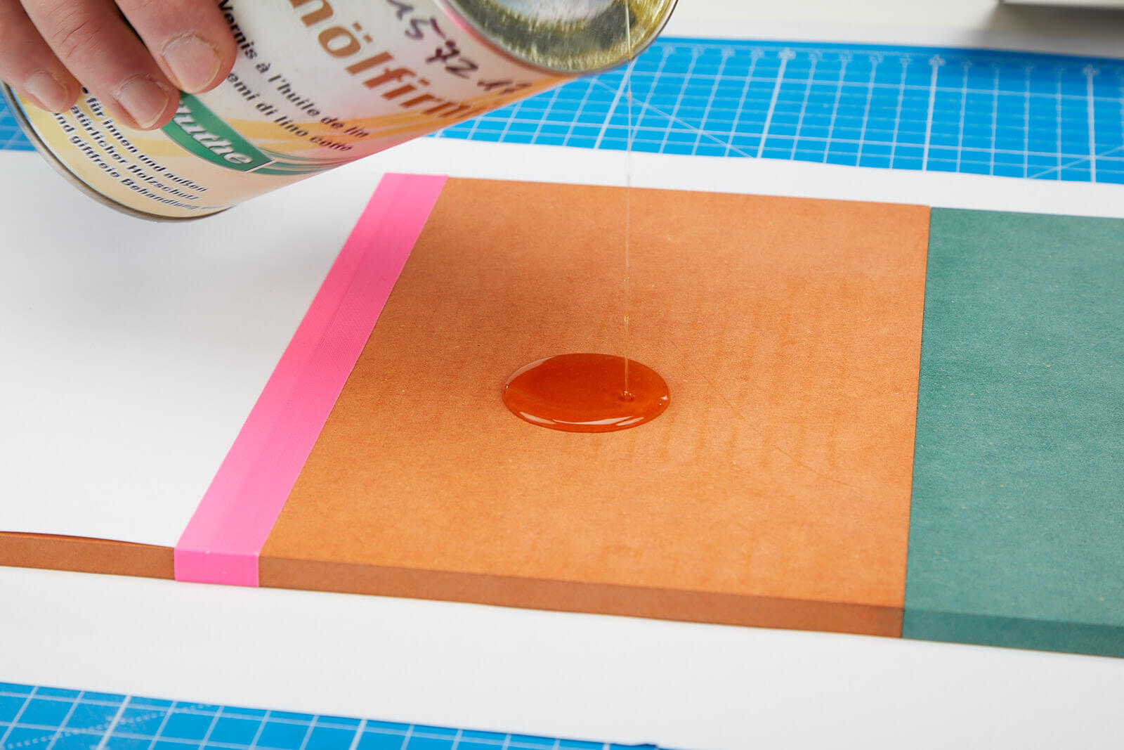 Auf eine orangene MDF.Platte wird Leinölfirnis geträufelt.