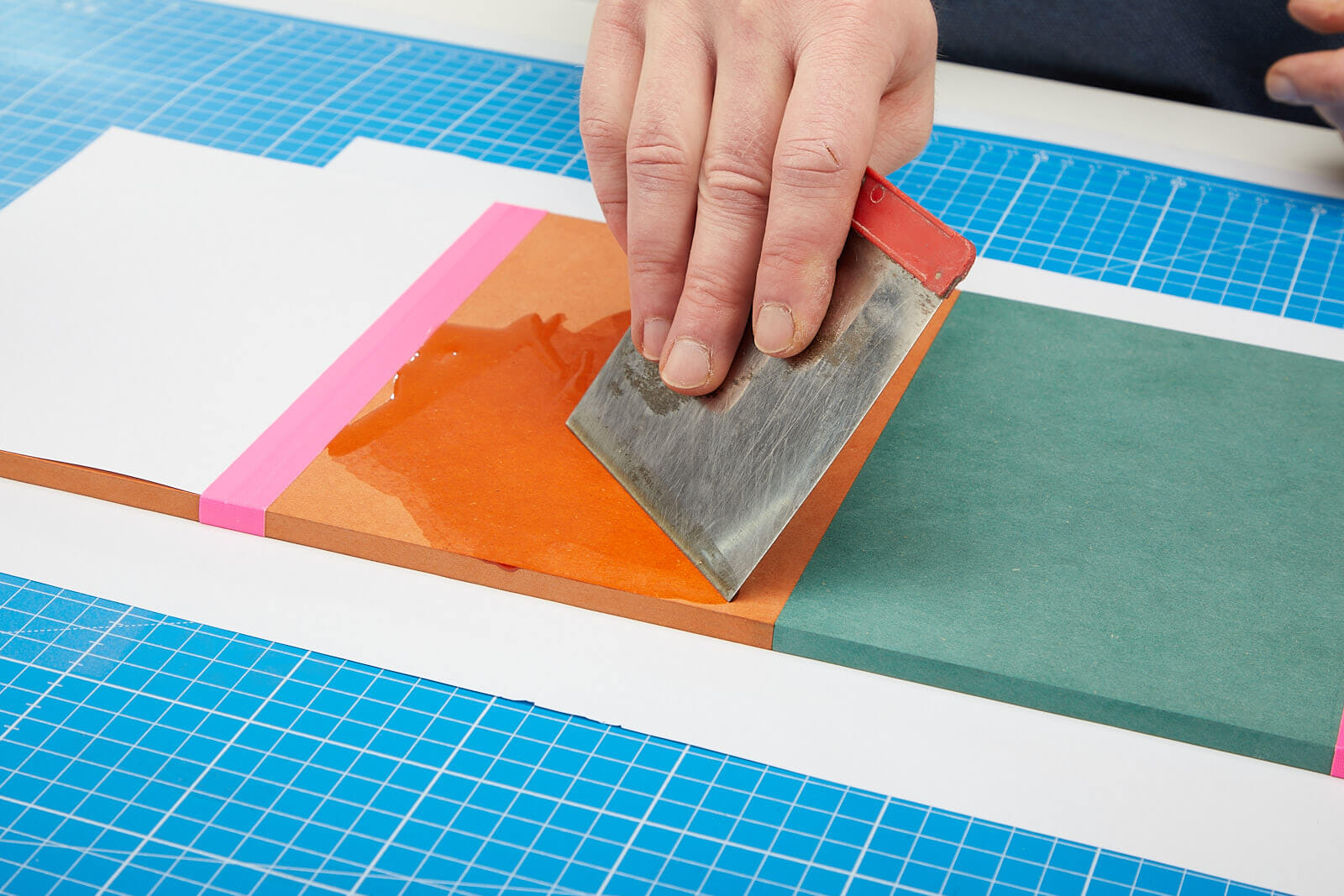 Mit einem Japanspachtel wird Öl auf orangenem MDF verteilt.