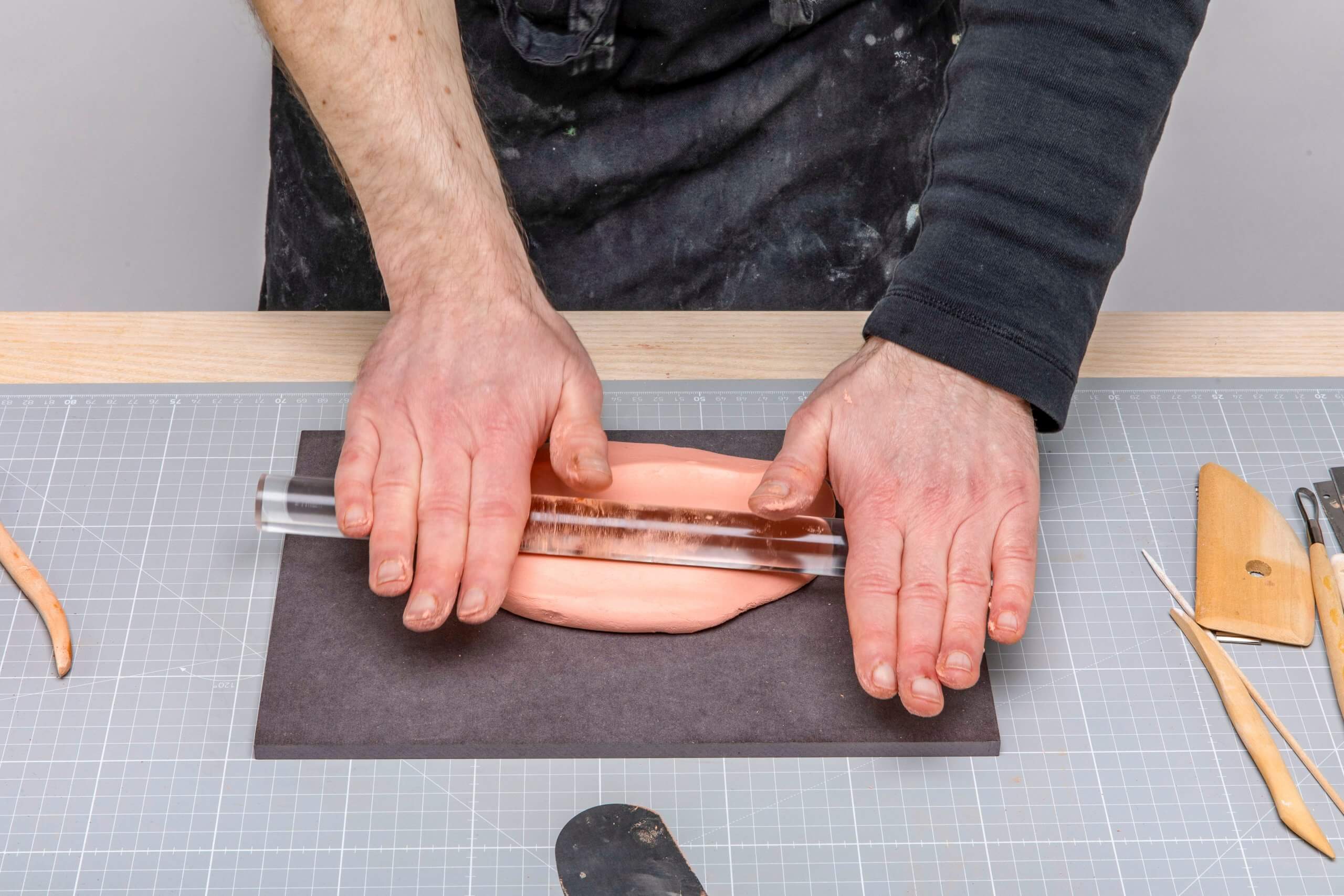 Hand-Abformmasse ausrollen Auf einem schwarzen Brett wird von zwei Haenden mit einem Acrylglasstab Modelliermasse ausgewalzt.
