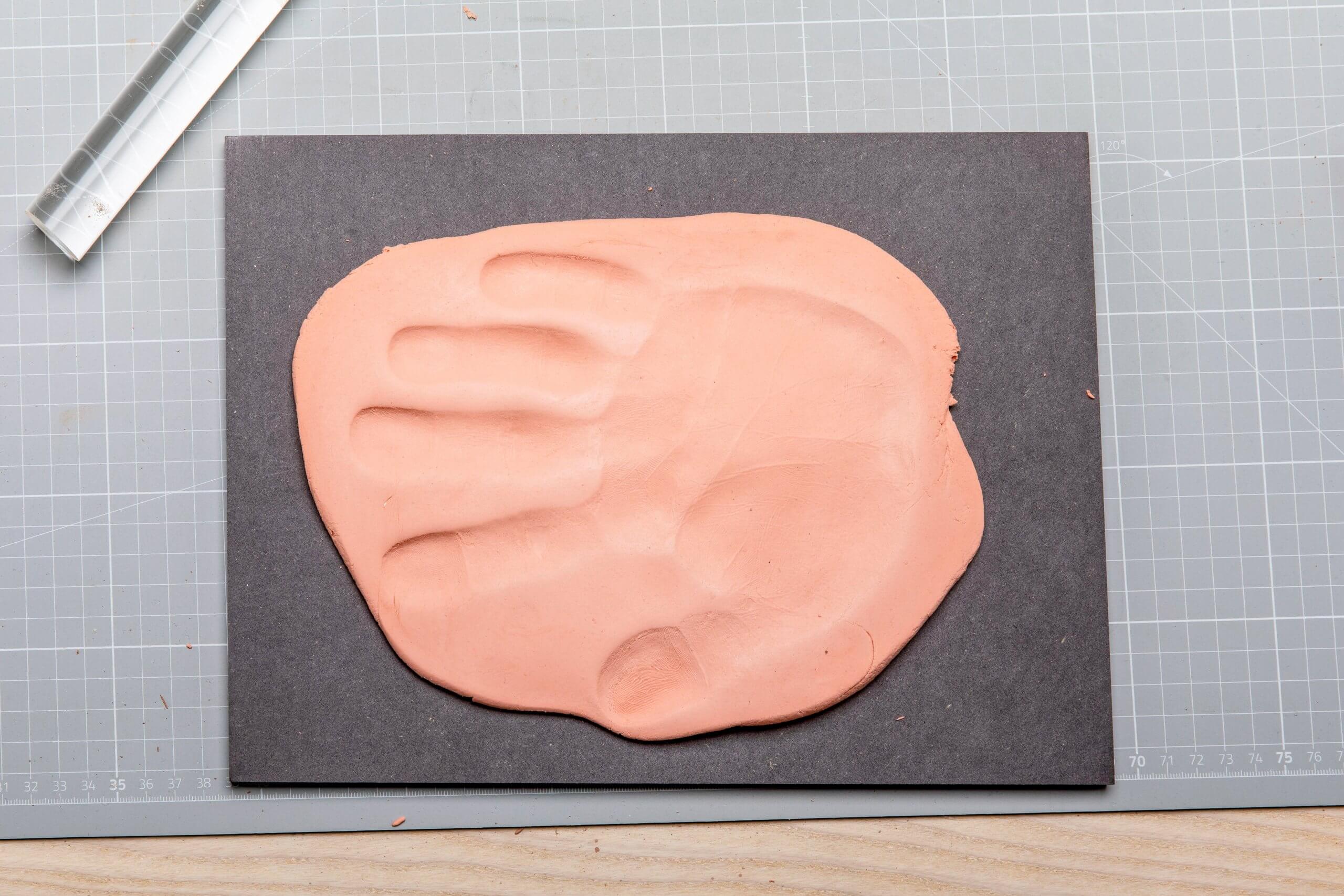 Handabdruck in Modelliermasse Auf einem schwarzen Brett liegt ein Handabdruck in hellrosa Abformmasse.