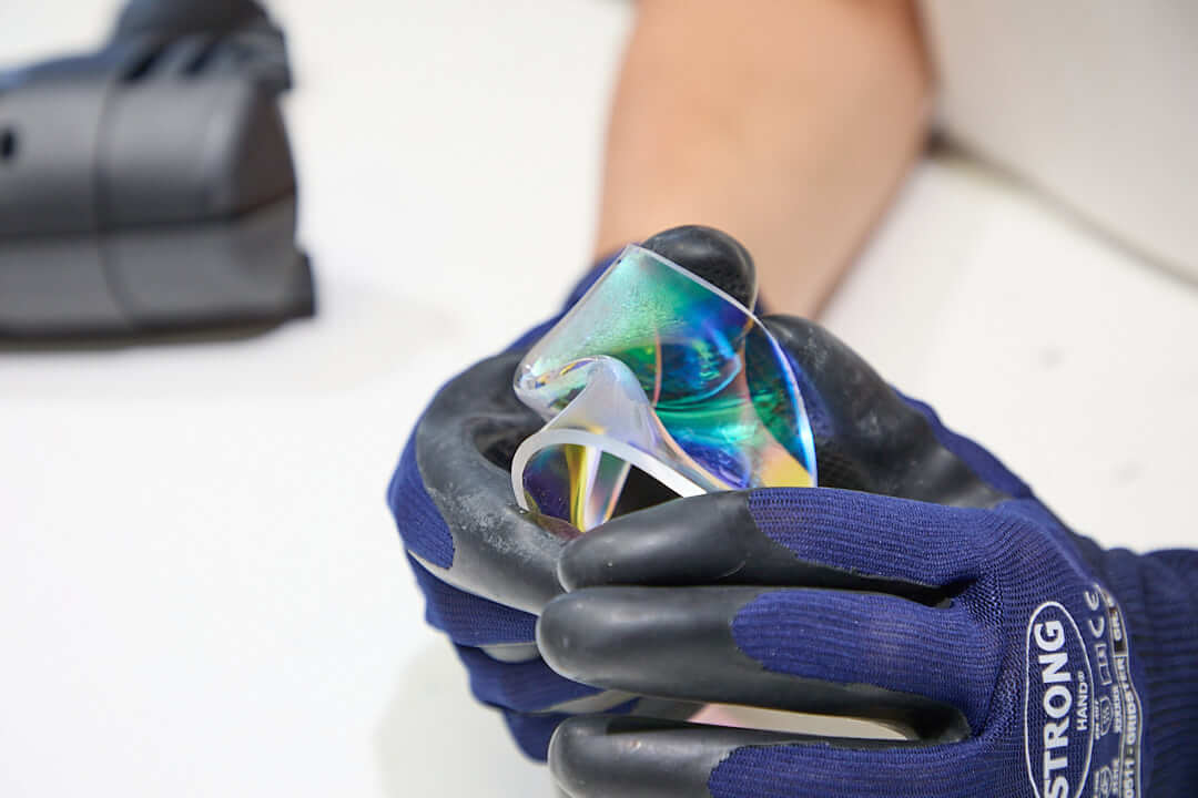 Acrylglas von Hand formen Zwei Hände in Schutzhandschuhen formen eine erwärmte Acrylglasscheibe. Das irisierende Acrylglas ist stark verformt (gebogen) und zeigt auf den gekrümmten Flächen verschiedenfarbige Lichtreflexionen.