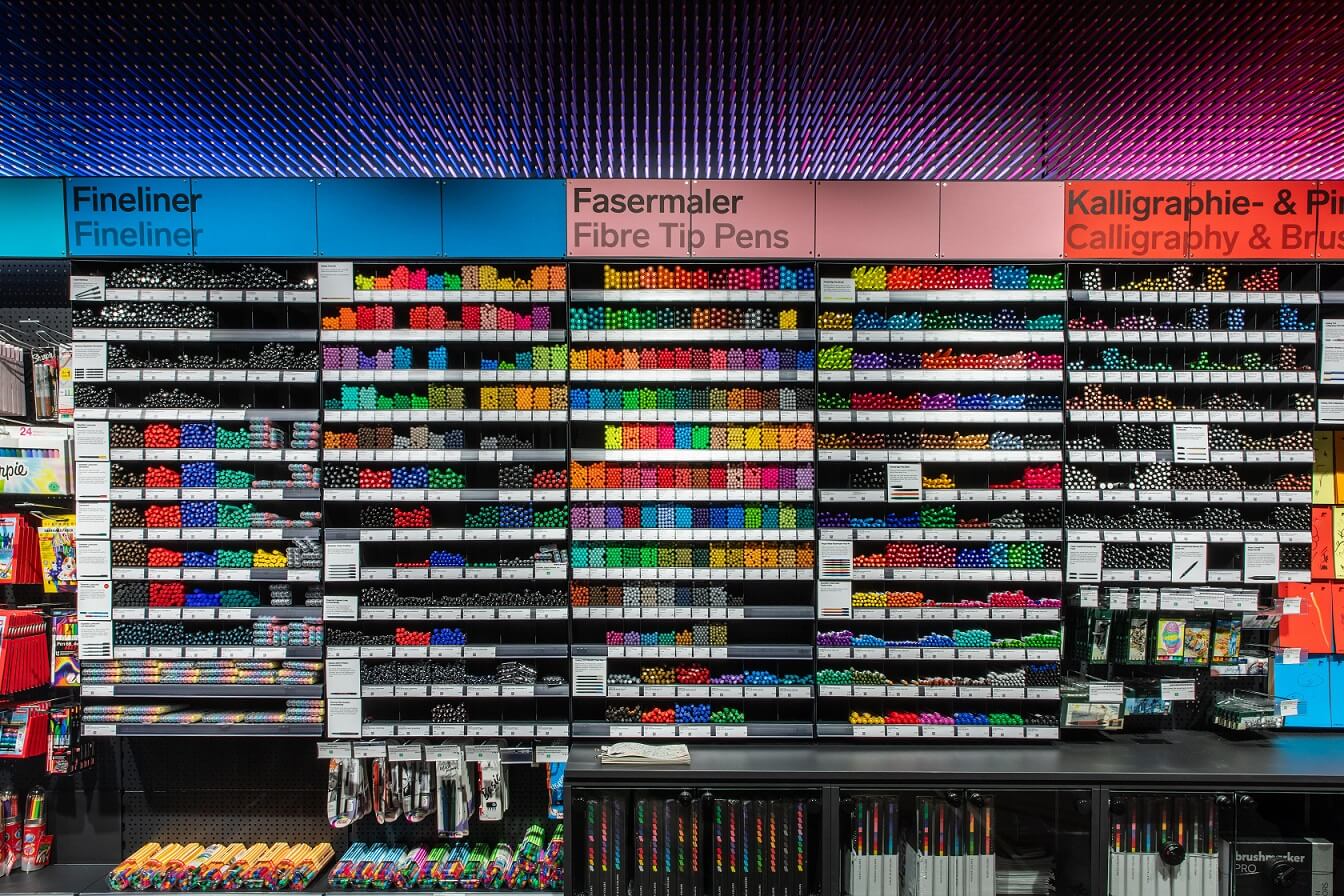 Ausschnitt Stifteregal, frontal Ein Ausschnitt der Stiftewand ist zu sehen. Im Bild sind die Regalfächer, die mit "Fineliner", "Fasermaler" und "Kalligraphie" überschrieben sind.